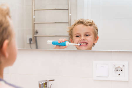 A five-year-old boy is brushing his teeth in the bathroom. A five-year-old boy, a European on the street, brushes his teeth in the bathroom in front of the mirror.の写真素材