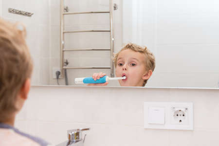 A five-year-old boy is brushing his teeth in the bathroom. A five-year-old boy, a European on the street, brushes his teeth in the bathroom in front of the mirror.の写真素材