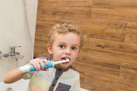 A five-year-old boy is brushing his teeth in the bathroom. A five-year-old boy, a European on the street, brushes his teeth in the bathroom in front of the mirror.の写真素材