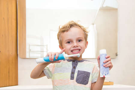 A five-year-old boy is brushing his teeth in the bathroom. A five-year-old boy, a European on the street, brushes his teeth in the bathroom in front of the mirror.の写真素材