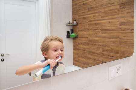 A five-year-old boy is brushing his teeth in the bathroom. A five-year-old boy, a European on the street, brushes his teeth in the bathroom in front of the mirror.の写真素材