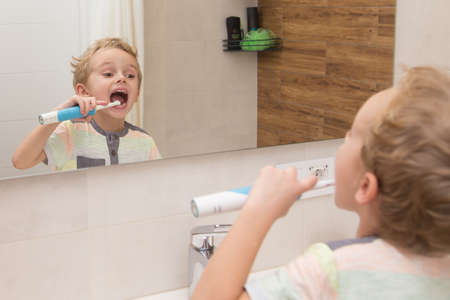 A five-year-old boy is brushing his teeth in the bathroom. A five-year-old boy, a European on the street, brushes his teeth in the bathroom in front of the mirror.の写真素材
