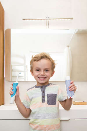A five-year-old boy is brushing his teeth in the bathroom. A five-year-old boy, a European on the street, brushes his teeth in the bathroom in front of the mirror.の写真素材
