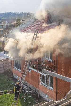 Firemen fighting a raging fire with huge flames of burning timber.Fire in a country house. Firefighters extinguish two-story brick building.の写真素材