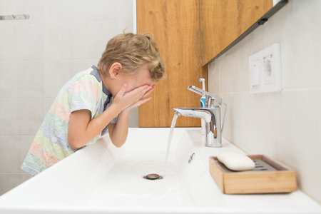 A five-year-old boy washes his hands in the bathroom. A boy of five years old, European outside washes his hands in the bathroom in front of the mirrorの写真素材