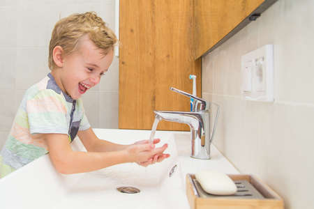 A five-year-old boy washes his hands in the bathroom. A boy of five years old, European outside washes his hands in the bathroom in front of the mirrorの写真素材