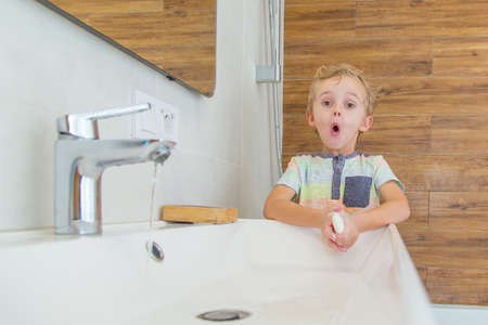 A five-year-old boy washes his hands in the bathroom. A boy of five years old, European outside washes his hands in the bathroom in front of the mirrorの写真素材