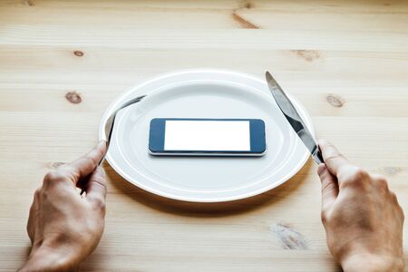 man's hand with a fork and knife cut smartphoneの写真素材