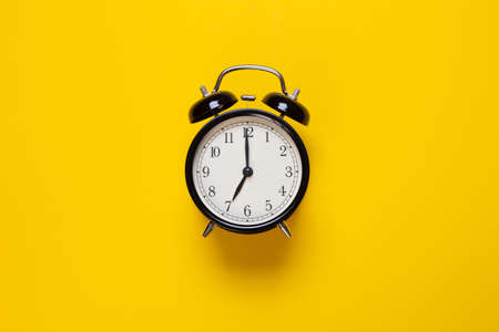 alarm clock shows 7 o'clock on a yellow backgroundの写真素材