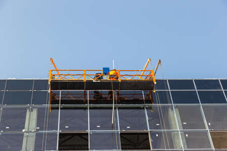 Workers on the aerial work platform at facade installation workの写真素材