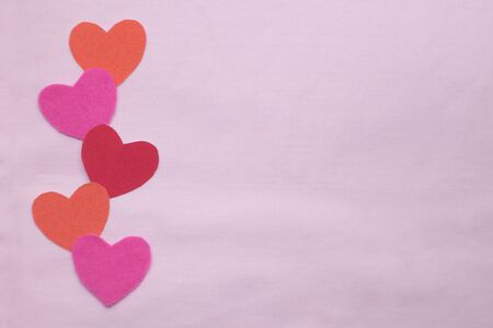 Colored hearts lie on a pink background. Copy space.