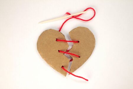 Broken cardboard heart stitched with red thread on the withe background.の写真素材