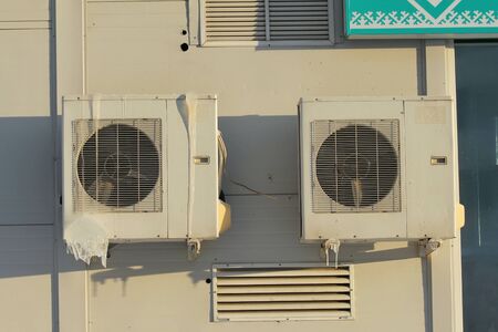 Two air conditioners on a white wall with icicles.