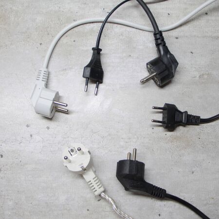 Electric plugs with cords lie on a gray surface in a circle.