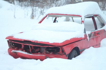Old disassembled car on a city street in winter covered with snow.の写真素材