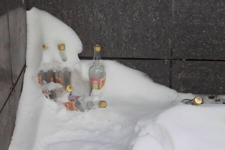 Glass bottles from alcohol and carbonated drinks in snowdrift. Concept of cleaning city services. Alcohol and drug addiction. Stock photo with empty space for text.の写真素材