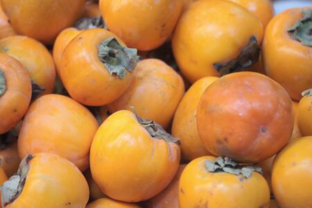 Red yellow juicy persimmon lie on a store counter.の写真素材