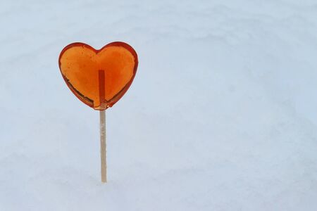 Red heart shaped lollipop sticks out of snow in winter.の写真素材