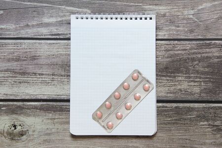 Notepad with a blank white sheet in a checker paper with pills in a blister lies on the background of wooden boards.の写真素材