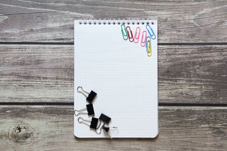 Notepad with a blank white sheet in a checker paper with a clip and with paper clips lies on the background of wooden boardsの写真素材