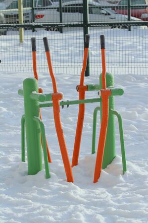 Outdoor fitness equipment on winter urban background, concept of active winter recreation, health care. Vibrant cheerful greens and oranges color. Stock photo with empty space for text.の写真素材