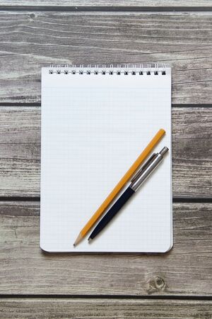 Notepad with a blank white sheet in a checker paper with ball pen and simple graphite pencil lies on the background of wooden boards.の写真素材