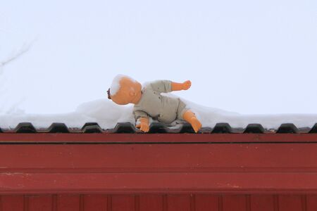 An old plastic doll with a soft cloth body thrown onto the roof of a house covered in snow. The concept of a dysfunctional childhood, mental child injuries. Stock photo with empty space for text.の写真素材