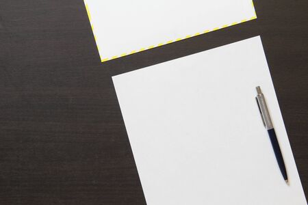 Template of white paper with pen and envelope on dark wenge color wooden background. Concept of business plan and strategy. Stock photo with empty space for text and design.の写真素材