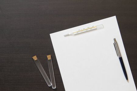 Template of white paper with pen, bottle and thermometer on dark wenge color wooden background. The provision of medical and pharmacological services. Stock photo with empty space for text.の写真素材
