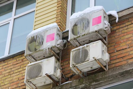 Four white conditioning part of a split system hanging on a brick wall of a building covered in snow and icicles in winter in Russia.の写真素材