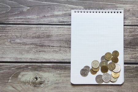Notepad with a blank white sheet in a checker paper with russian coins lies on the background of wooden boards.の写真素材