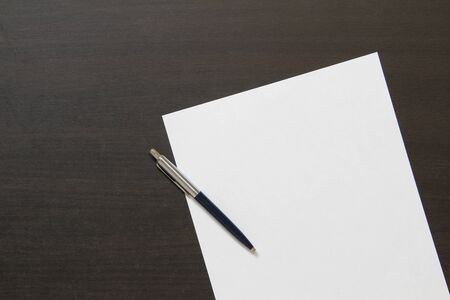 Template of white paper with pen on dark wenge color wooden background. Concept of business plan and strategy. Stock photo with empty space for text and design.の写真素材