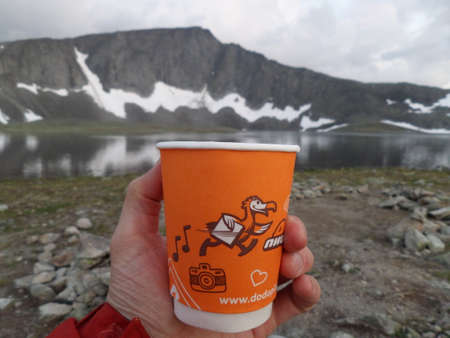 25 july 2017, Russia, Komi, Ural mountains. A paper cup with the logo of the international network of pizzerias Dodo pizza man holds in his hand an a background of mountains and a lake in the Ural Mountains.のeditorial素材