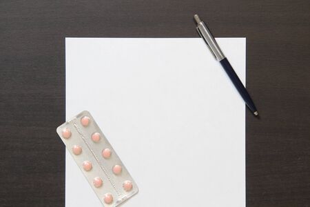 Template of white paper with pen and pills in a blister on dark wenge color wooden background. The provision of medical and pharmacological services. Stock photo with empty space for text and design.の写真素材