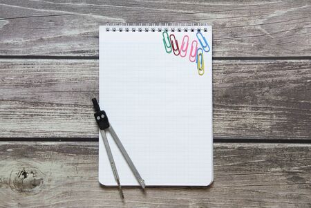 Notepad with a blank white sheet in a checker paper and with compass lies on the background of wooden boards.の写真素材