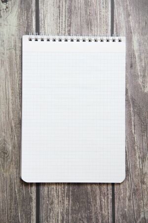 Notepad with a blank white sheet in a checker paper lies on the background of wooden boards