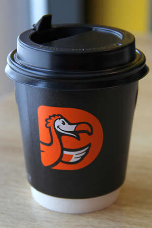 08-02-2020, Russia, Syktyvkar. Black paper coffee cup with black plastic lid and orange logo of the international pizzeria chain. Dodo pizza is on the table near the window in the restaurant.のeditorial素材
