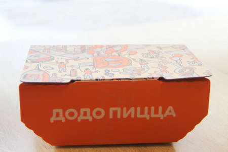 08-02-2020, Russia, Syktyvkar. Orange cardboard company box for Dodo snacks with a side inscription pizza and a corporate design and logo on the lid is standing on a table in a restaurant near the window.のeditorial素材
