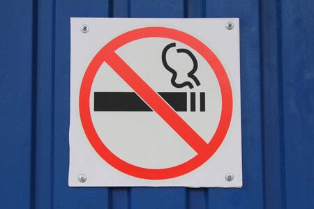 On the blue wall there is a white sign with an inscription prohibiting smoking. The concept of health and prohibition.の写真素材