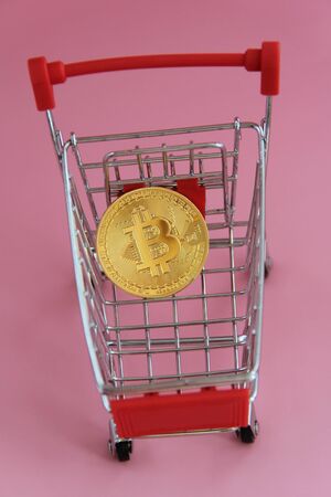 Gold coin with the image of bitcoin lies in the shopping basket.の写真素材