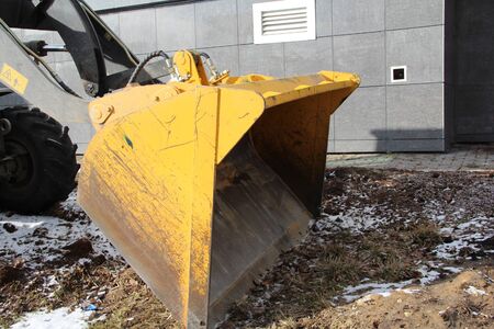 Yellow tractor knife on the ground against the background of a house in the city.