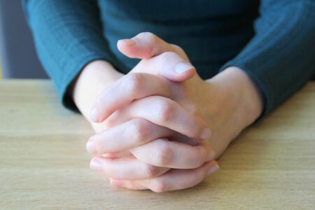 Palms folded in prayer. Clasped fingers. Girl sits and holds hands in front of her hands clasped...