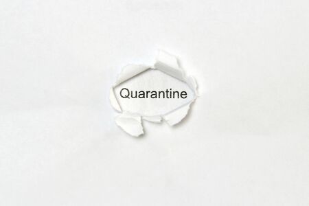 The word quarantine printed in black letters on a white sheet of paper is visible in a hole torn in another sheet of paper.の写真素材