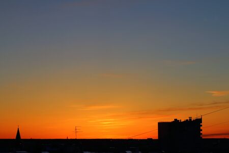 Sun below the horizon and television antenna, roof of a multi-storey urban building in the background fiery dramatic orange sky at sunset or dawn backlit by the sun. Place for text and design.の写真素材