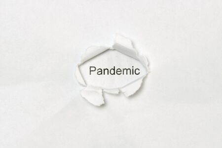 The word pandemic printed in black letters on a white sheet of paper is visible in a hole torn in another sheet of paper.の写真素材