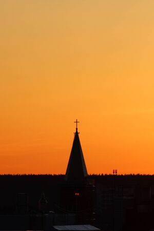 Sun below the horizon and the roof of the church with a cross on the background fiery dramatic orange sky at sunset or dawn backlit by the sun. Place for text and design.の写真素材