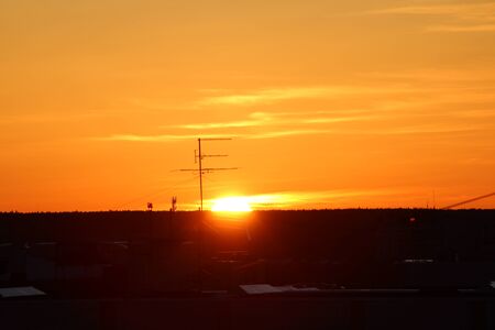 Sun over the horizon and television antenna in the background clouds in the orange sky at sunset or dawn backlit by the sun. Place for text and design.の写真素材