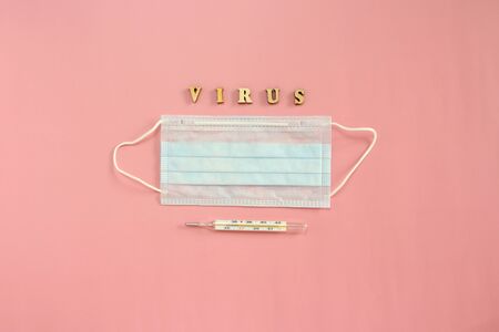 Medical disposable mask, thermometer and wooden letters forming the word Coronovirus on a pink background.の写真素材
