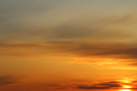 Sun below the horizon and clouds in the fiery dramatic orange sky at sunset or dawn backlit by the sun. Place for text and design.の写真素材