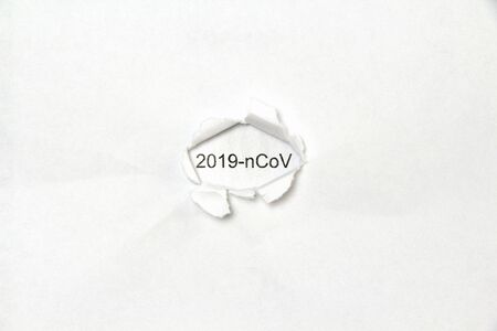 The word 2019-ncov printed in black letters on a white sheet of paper is visible in a hole torn in another sheet of paper.の写真素材